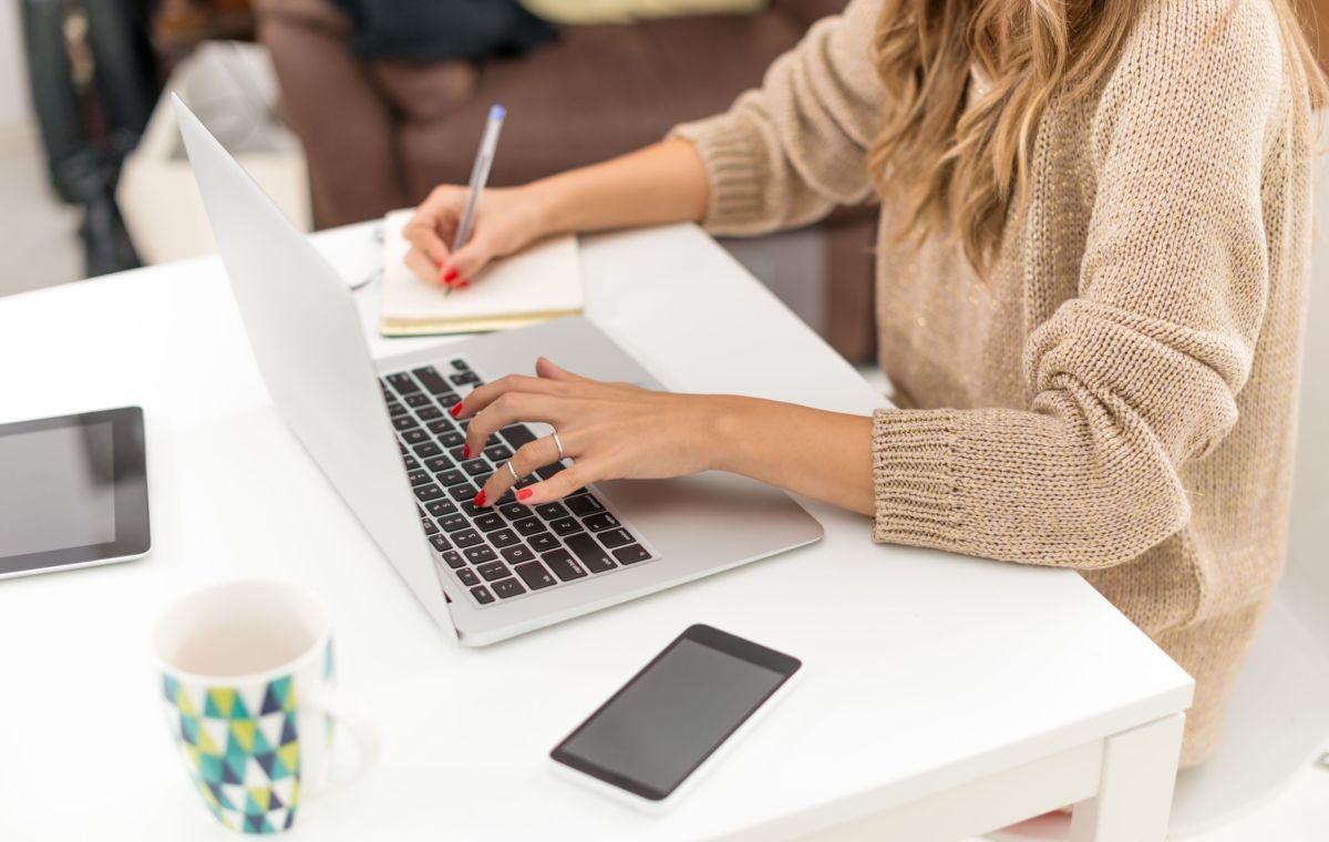 woman typing on laptop and writing note
