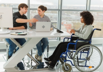 Une employée en fauteuil roulant discute avec ses collègues dans un bureau lumineux.