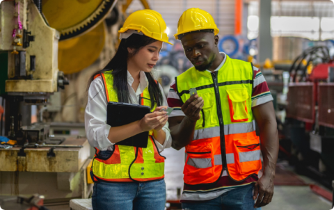 Two industrial workers inspecting a part on a factory floor.