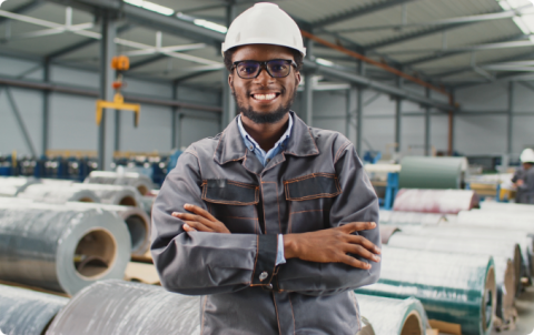 A smiling industrial factory worker wearing a hard hat and safety glasses.