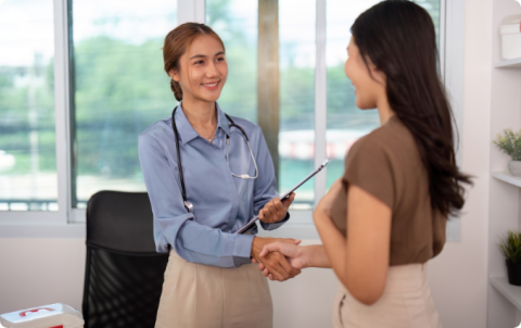 A female healthcare professional shaking hands with a patient during a consultation.