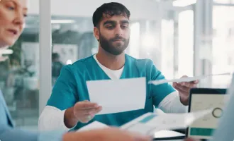 A healthcare worker in teal scrubs handling documents at a clinic desk.